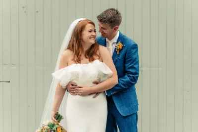 Bride and groom laughing together against a pale wall
