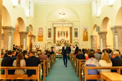 Interior of the Church of the Assumption in Booterstown, granite columns and rounded arches above a teal carpeted aisle, a groomsman walking towards the altar