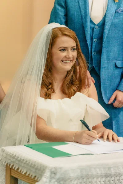 Bride signing the wedding register in the church, the groom standing behind her