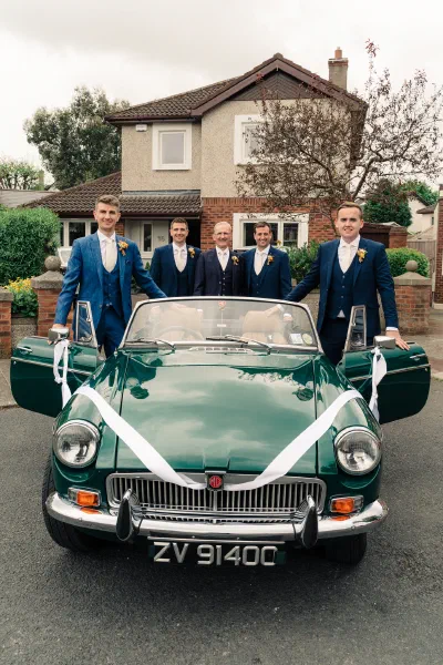 Groom and four groomsmen in blue suits standing behind a vintage green MG convertible outside a house in Dublin
