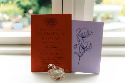 Terracotta wedding invitation with a dahlia line drawing reading Barbara and Declan, 19th May 2023, beside a lilac card with a poppy illustration