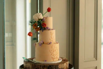 Three tier buttercream wedding cake with piped botanical detail and fresh tulips, on a wooden slice