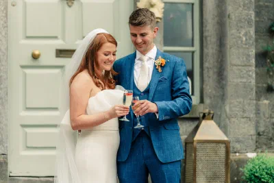 Bride and groom clinking champagne glasses in a painted doorway at The Millhouse in Slane
