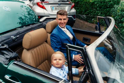 Groom sitting in the vintage green MG with a small boy at the steering wheel beside him
