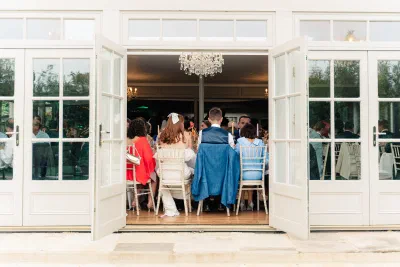 The orangery at The Millhouse seen from the garden in the evening, doors open, chandeliers lit and guests seated inside