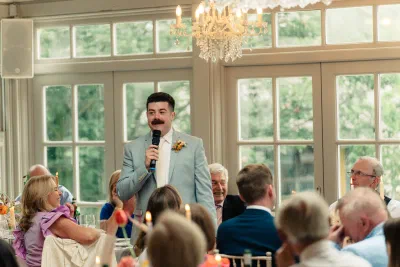 Guest giving a speech in the orangery at The Millhouse, seated guests laughing around the tables