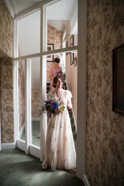 Bride at the top of the staircase at Orlagh House carrying a wildflower bouquet, bridesmaid behind her