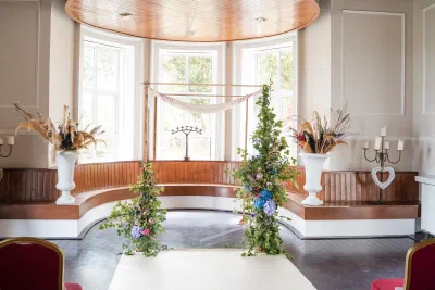 Wedding ceremony arch draped in linen and dressed with blue and purple wildflowers in the bay window at Orlagh House