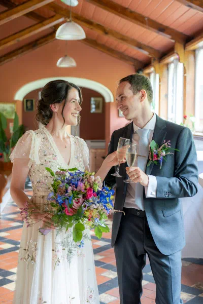 Bride and groom clinking champagne glasses in the beamed atrium at Orlagh House