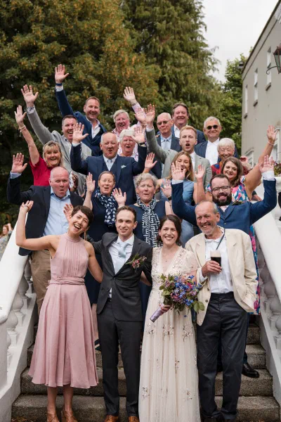 Wedding guests throwing their hands in the air for a group photograph on the steps at Orlagh House