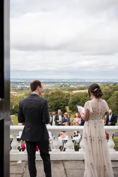 Bride and groom facing their guests from the terrace at Orlagh House, Dublin city on the horizon