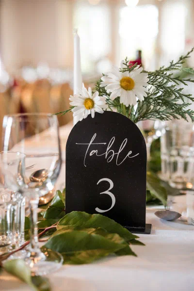 Black arched table number card with white calligraphy, daisies and foliage on a wedding table at Orlagh House