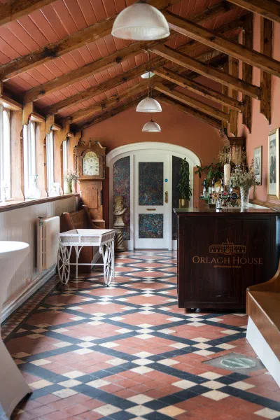 The tiled atrium corridor at Orlagh House with exposed beams, a grandfather clock and terracotta walls