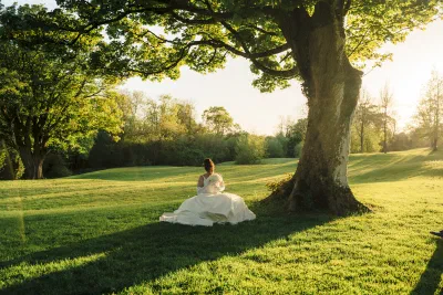 Bride sitting on the grass beneath the beech tree with her dress spread out around her