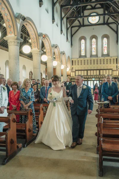 Bride walking up the aisle on her father’s arm as guests turn to watch