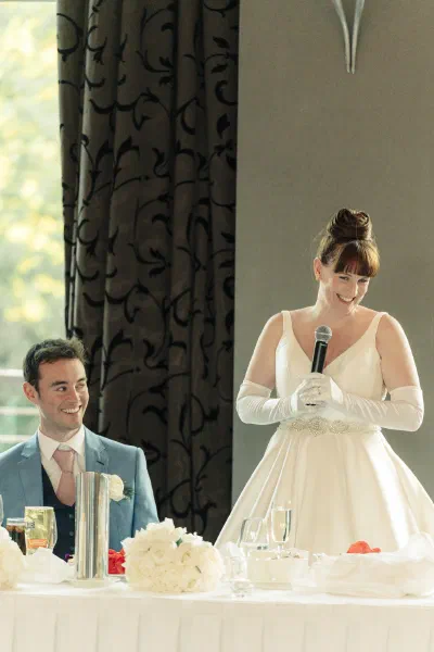 Bride standing to give her own speech, holding the microphone in her gloved hand