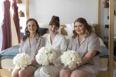 Four bridesmaids in matching pyjamas sitting on a four poster bed holding white peony bouquets
