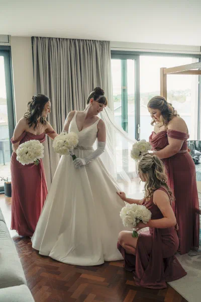 Bridesmaids in dusty rose kneeling to arrange the train of the wedding dress