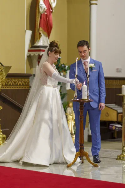 Bride lighting the wedding candle at the altar while the groom watches