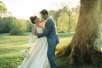 Bride and groom holding each other beneath the trunk of a mature beech tree in golden evening light
