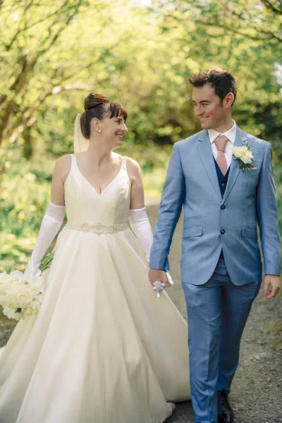 Bride and groom walking a green lane in dappled sunlight, holding hands