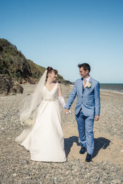 Bride and groom walking hand in hand across the shingle, her train dragging behind her