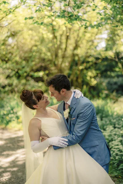 Bride and groom embracing on a narrow wooded lane thick with wild garlic