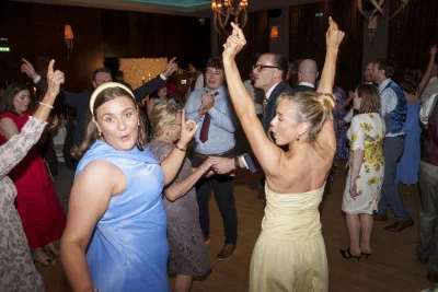 Packed wedding dancefloor with arms in the air under coloured lighting