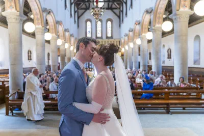 Bride and groom kissing at the top of the aisle, the nave stretching behind them
