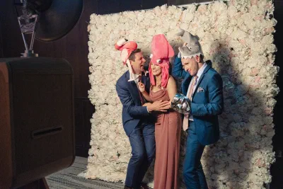 Guests in novelty hats posing against a white flower wall photo booth
