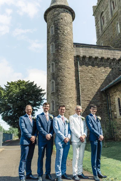 Groom and four groomsmen standing beneath the round stone tower of St Michael’s Church, Gorey