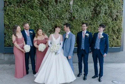 Full wedding party in dusty rose and navy standing along the ivy covered living wall at Seafield Hotel, the hotel name mounted on it