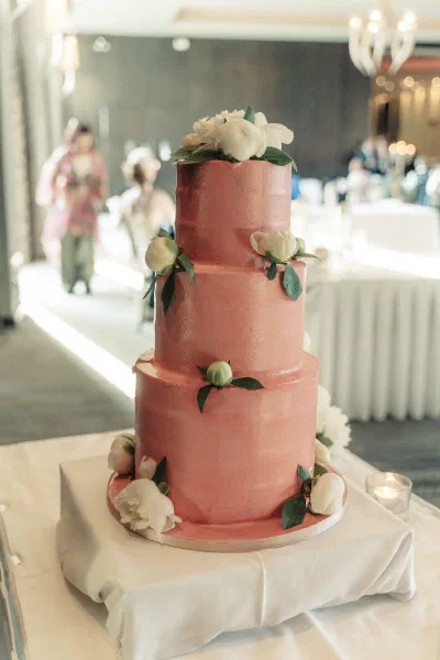 Three tier coral pink wedding cake decorated with white peonies