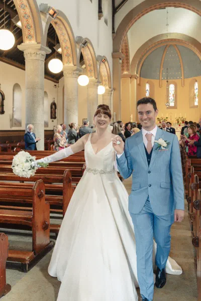 Newlyweds walking back down the aisle hand in hand, both laughing