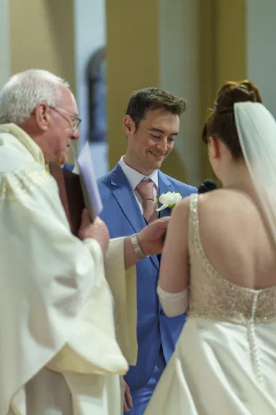 Close photograph of the ring exchange during the ceremony, the priest’s hands in frame